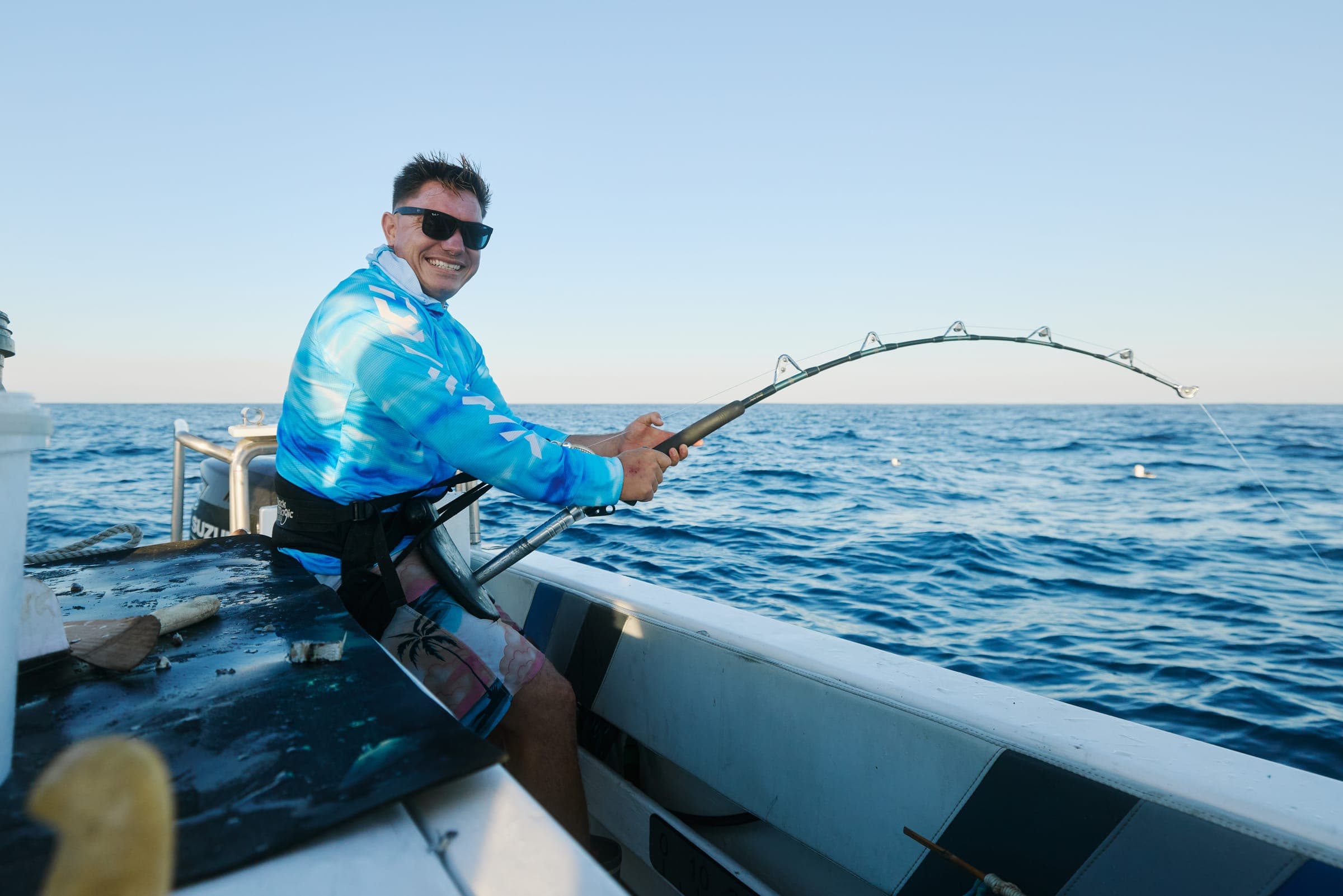 An angler in a fighting harness bracing against a rod loaded up with a running fish.
