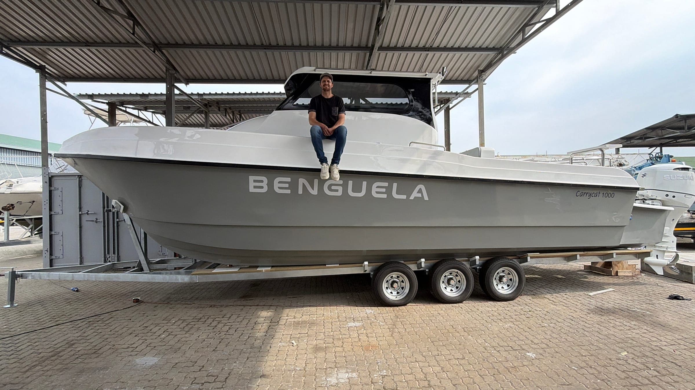 Benguela, a new Carrycat 1000 catamaran, on her trailer at the boatyard before delivery, with her name on the hull and the skipper sitting on the bow.