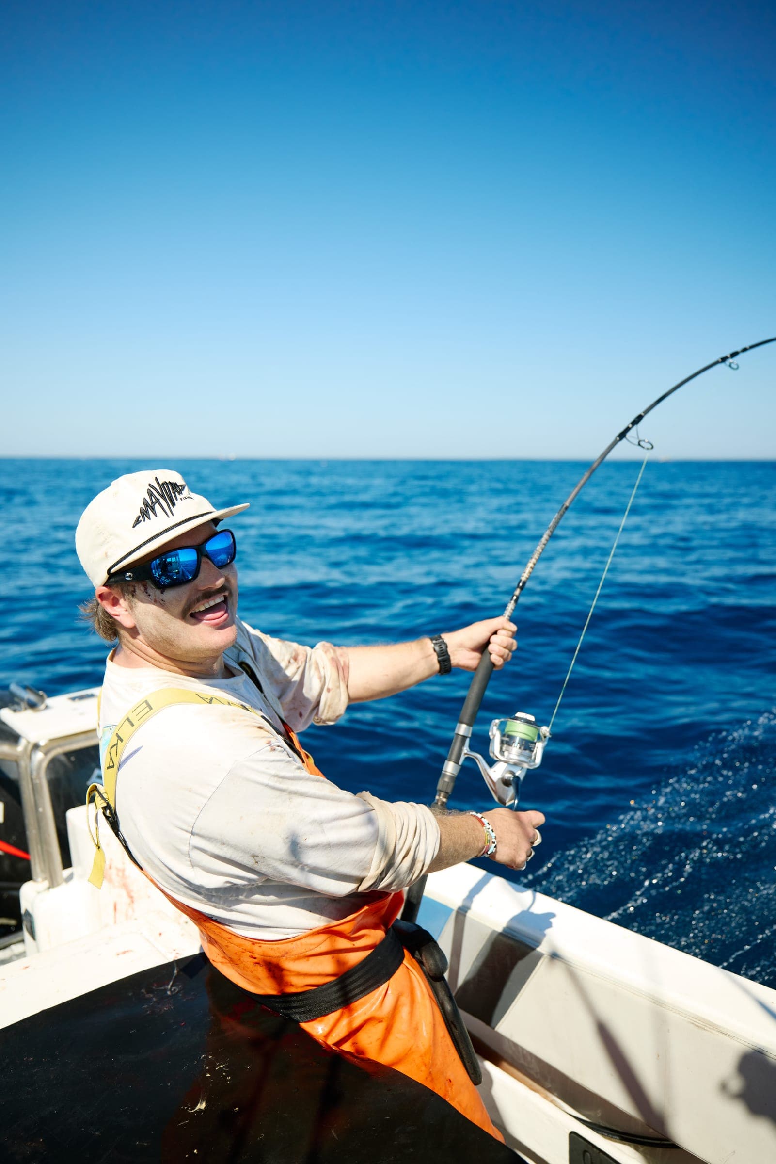 An angler smiling as the rod loads up, seen from low on the deck.