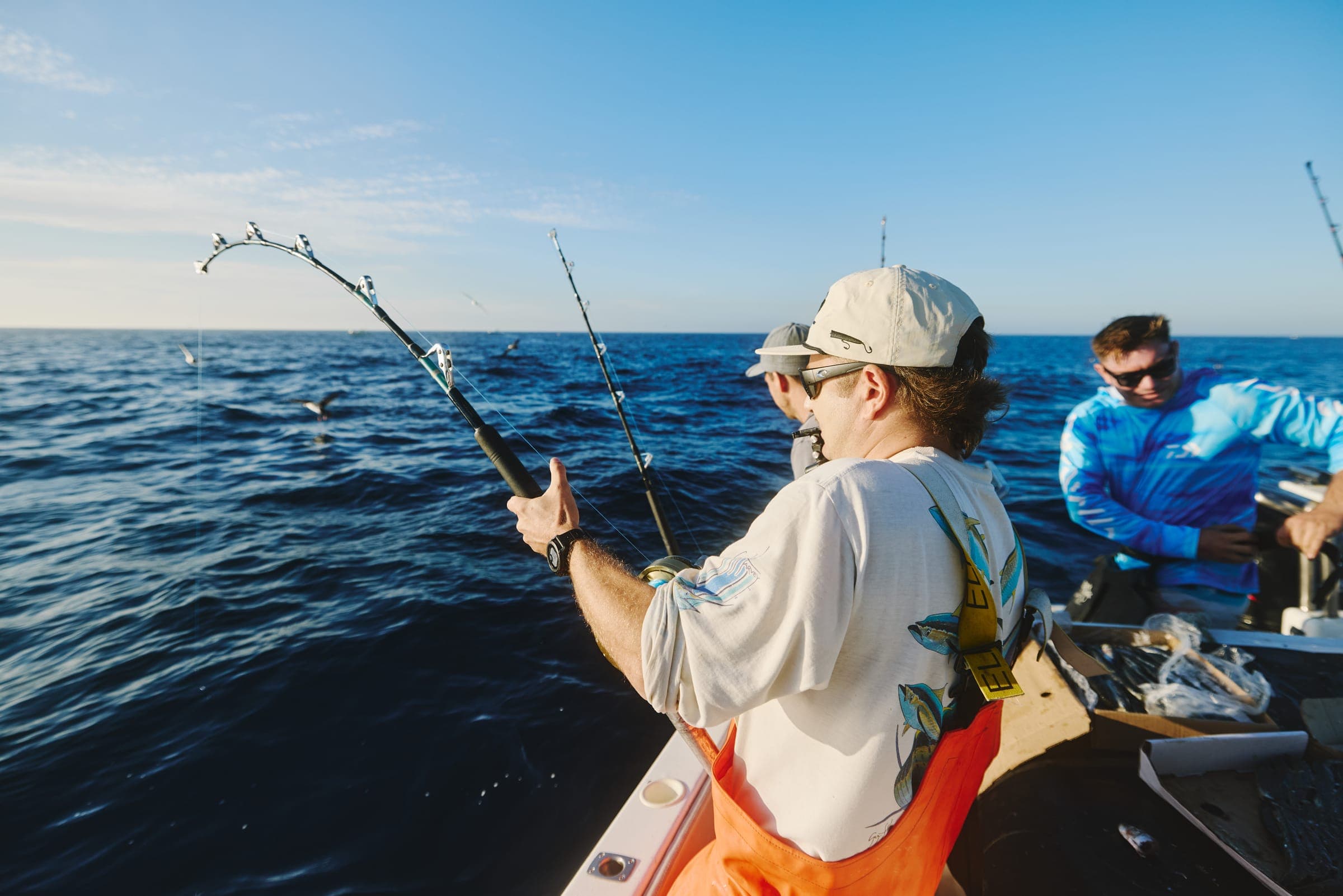 Seabirds working a bait shoal on the surface while two anglers fish from the deck.