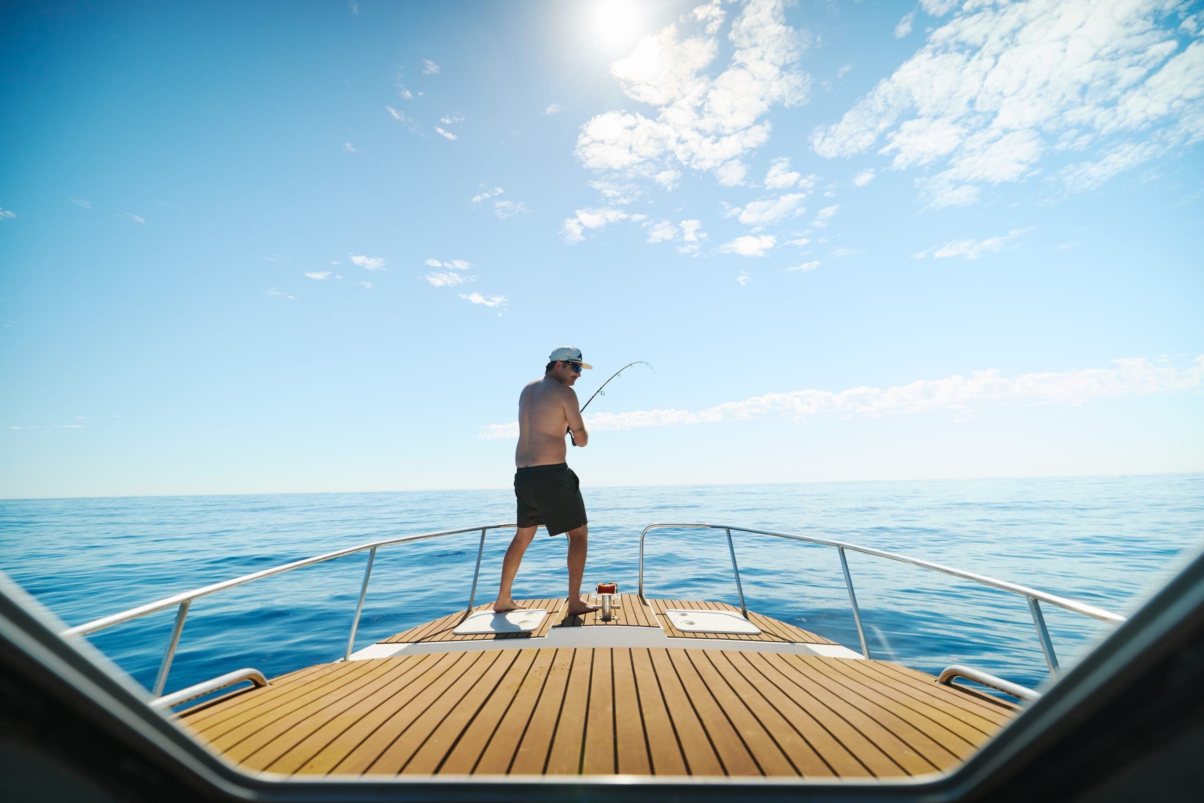 An angler casting from the teak bow deck on a flat, clear inshore day.