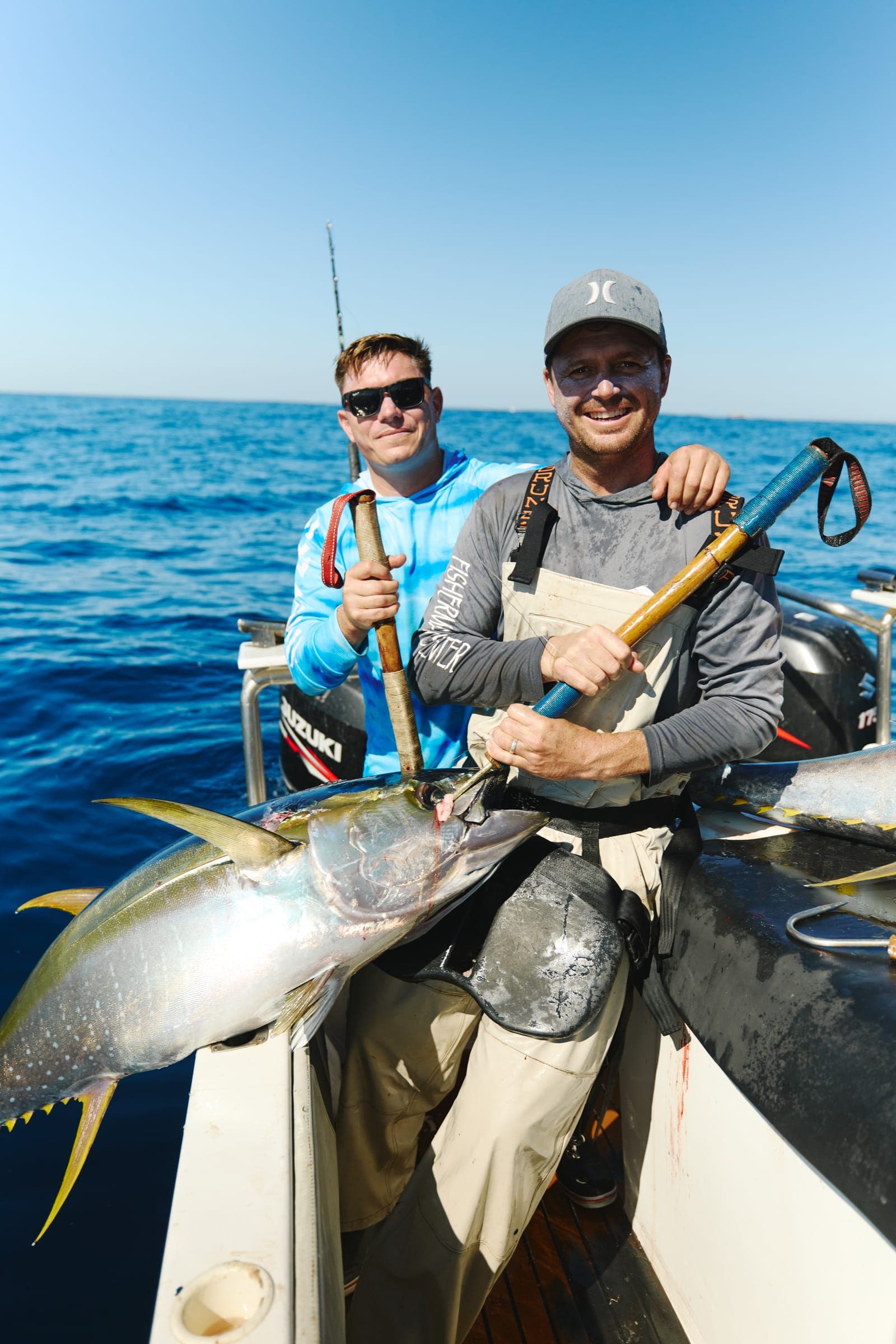Two crew lifting a yellowfin tuna over the gunwale with the open Atlantic behind them.