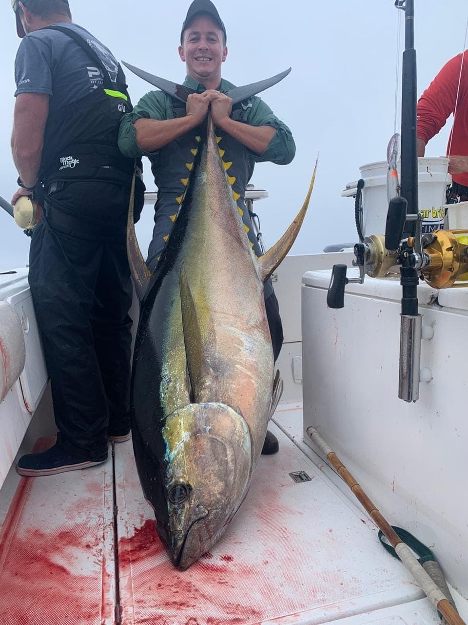 An angler standing a large tuna upright on the deck, taller than his waist.