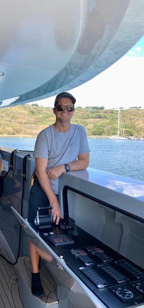Garreth standing in the cockpit of a boat at anchor, with green hills behind.
