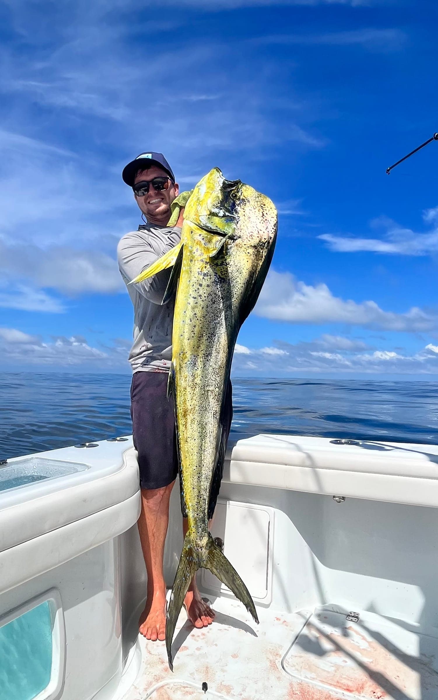 Garreth holding a dorado upright by the tail on a sunny day.