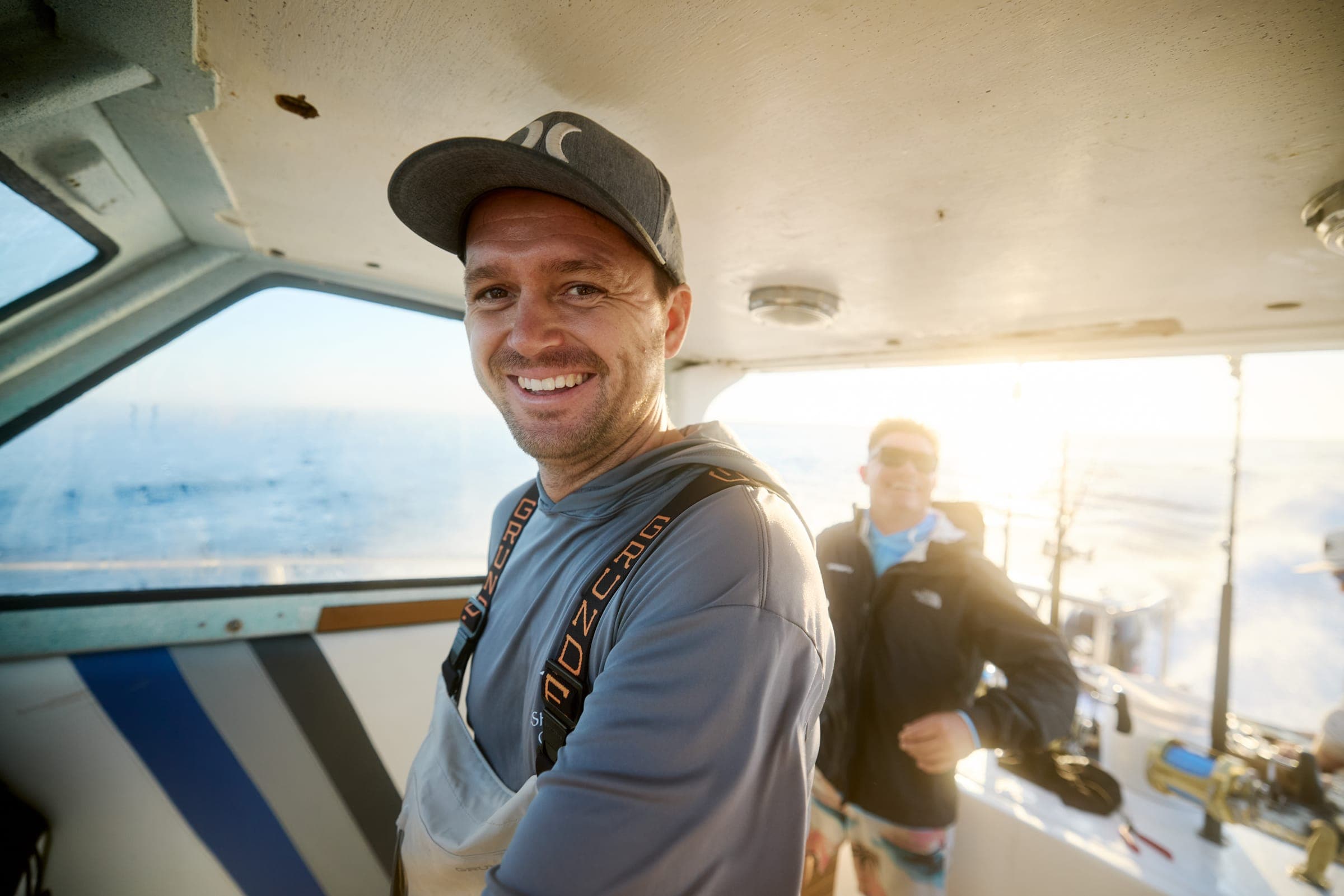 Garreth smiling in the cabin of a boat, with a crew member behind.