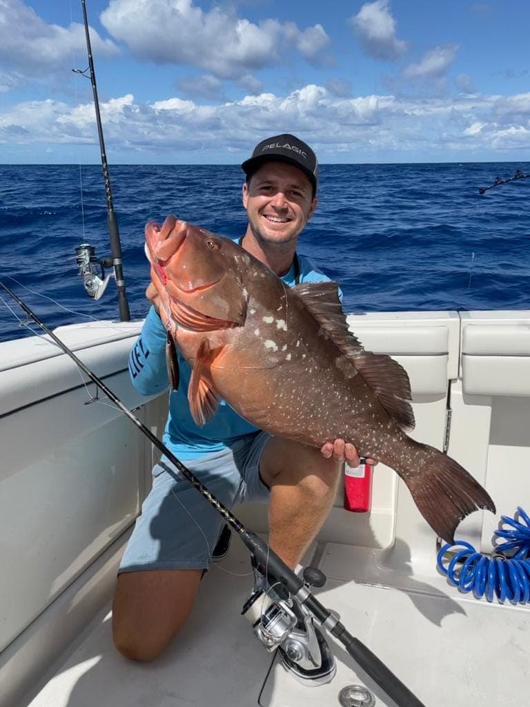 Garreth kneeling on a deck holding a large red reef fish.