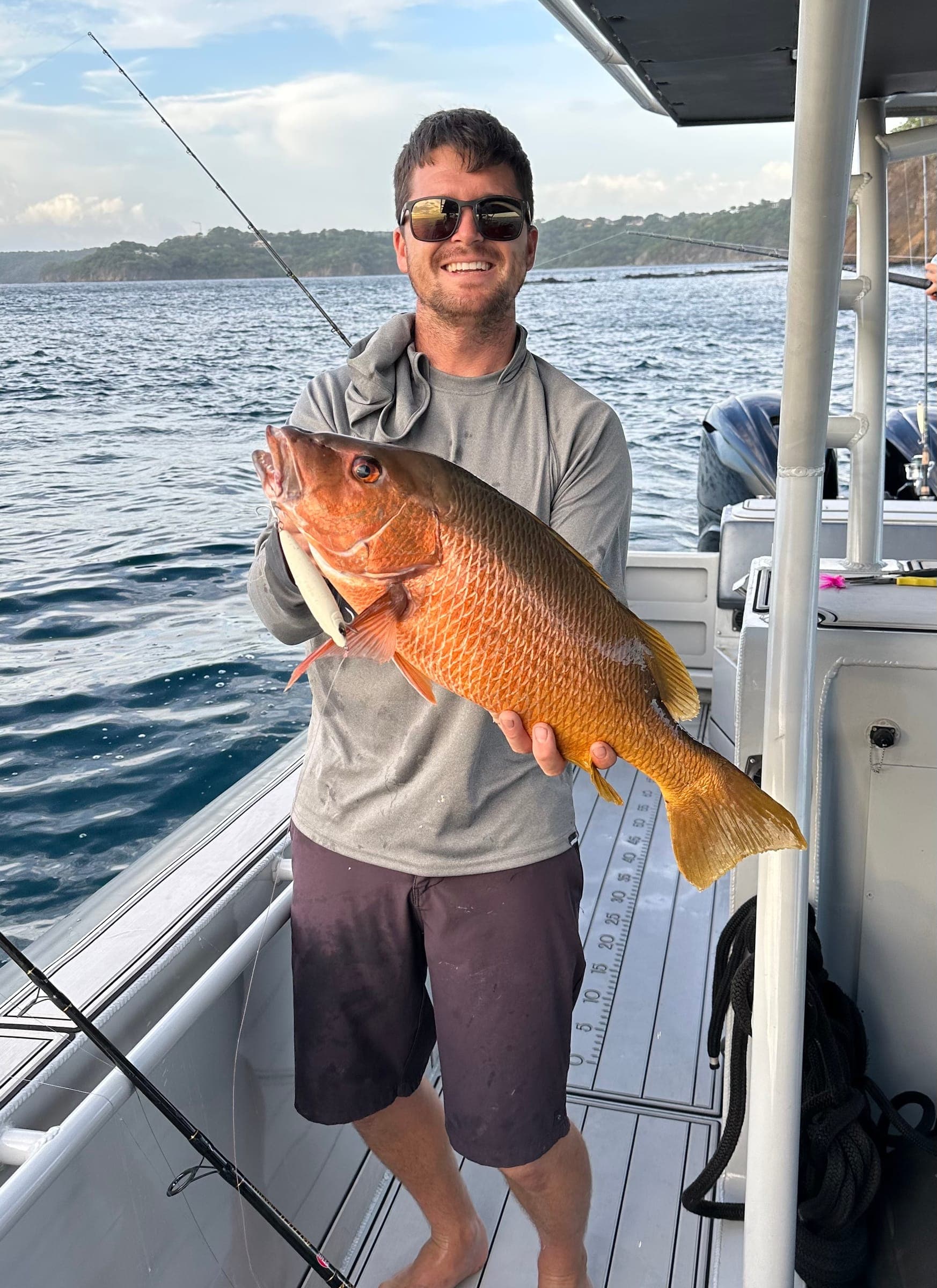 Garreth standing on a boat holding a red snapper-like fish.