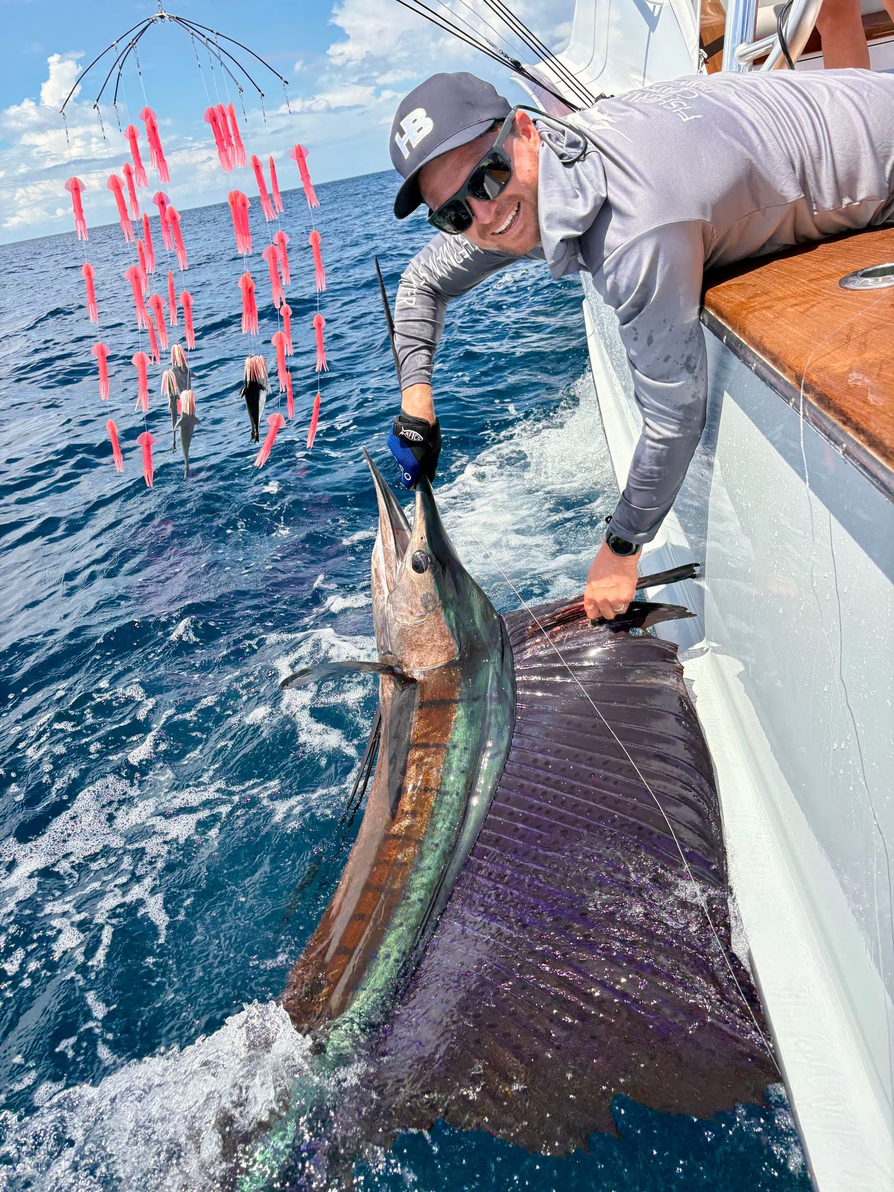 Garreth leaning over the side to a sailfish alongside, with teaser lures in the water.