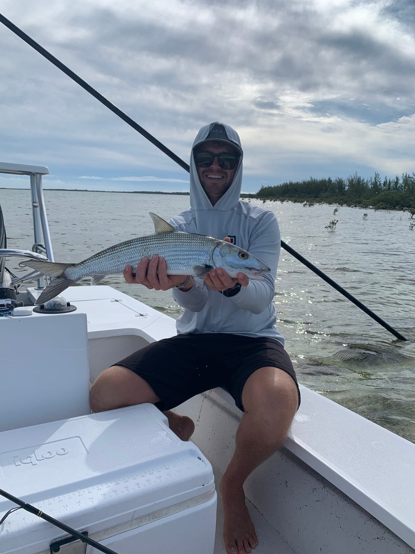 Garreth seated on a boat holding a silver fish under a cloudy sky.