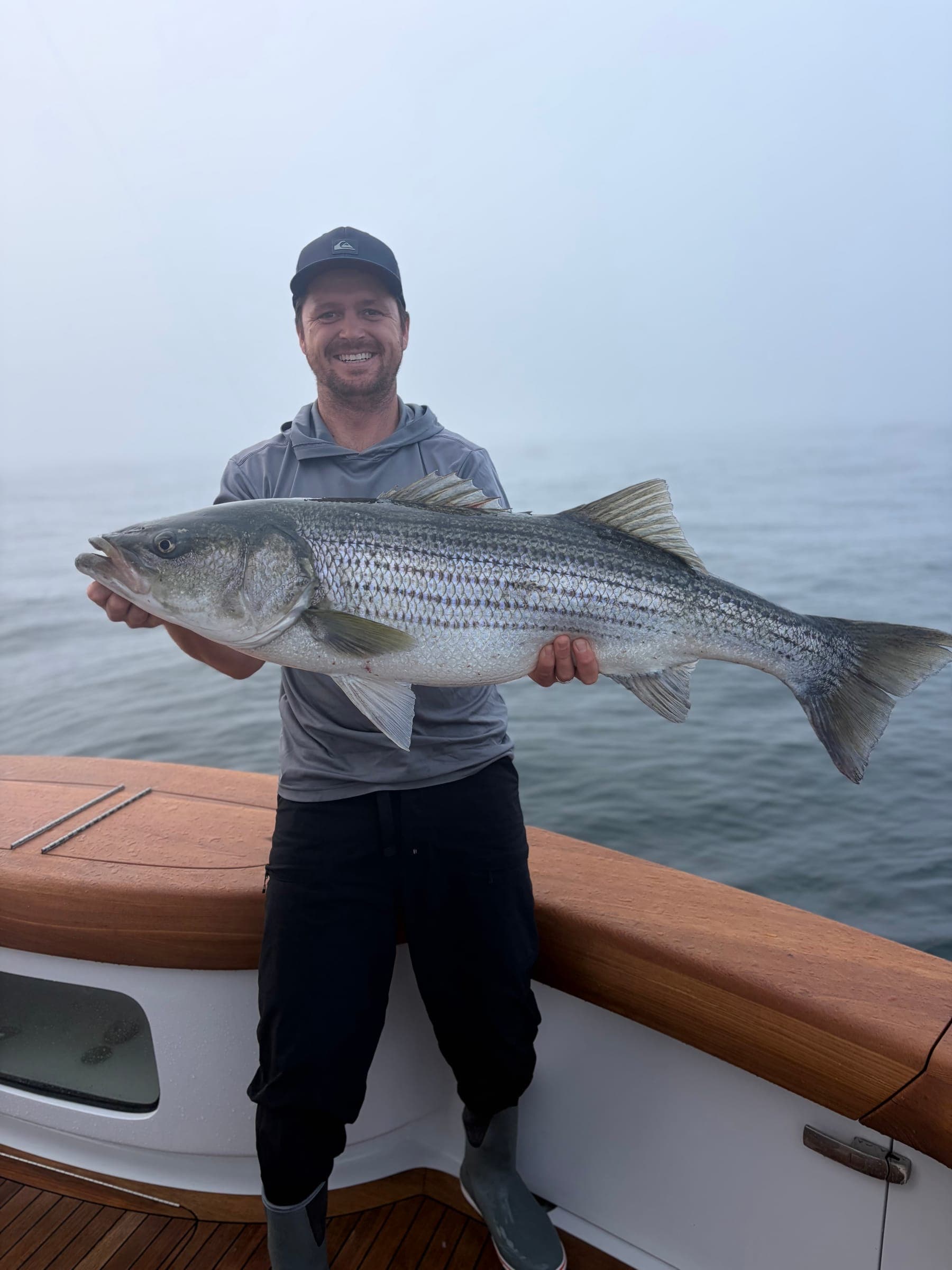 Garreth holding a large striped fish on deck in thick fog.