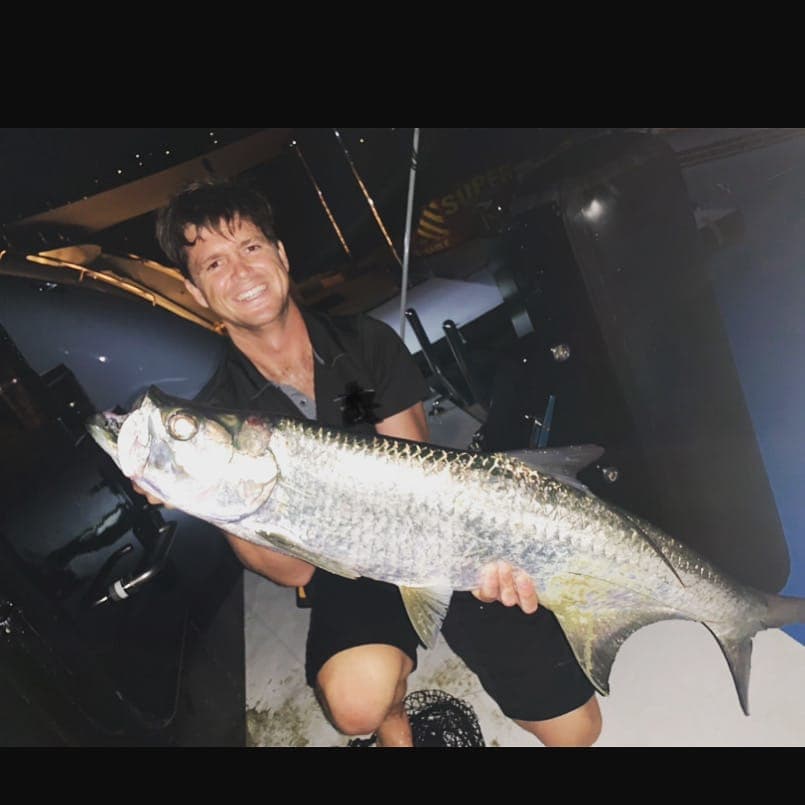 Garreth holding a large silver tarpon on deck at night.