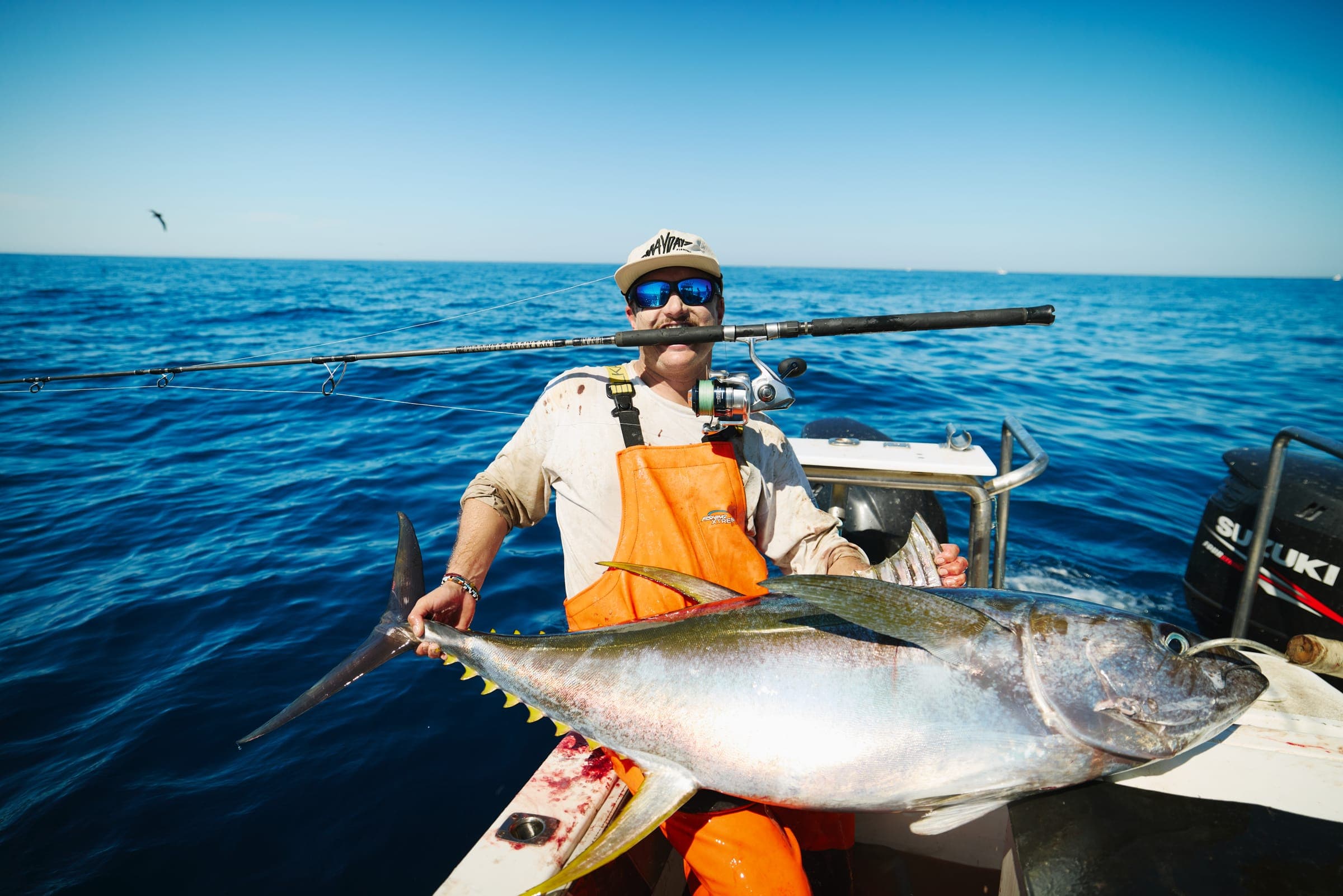 An angler in orange bibs holding a tuna at the rail on a bright day.