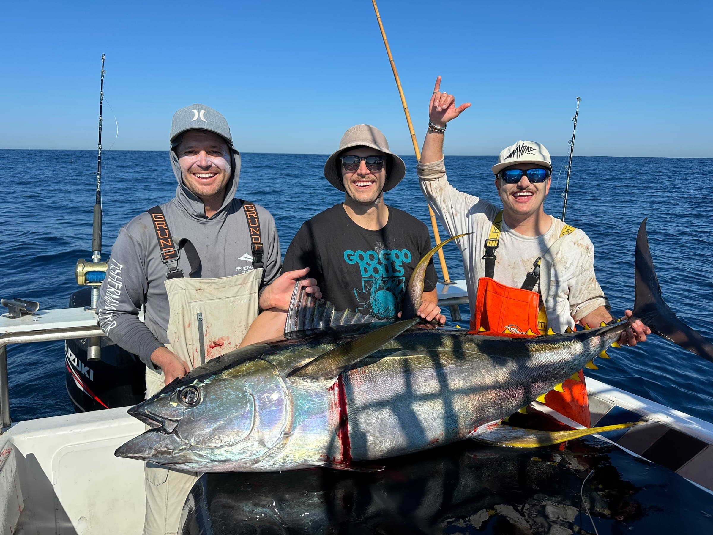 Three anglers behind a large yellowfin tuna laid across the gunwale, one with a hand raised.
