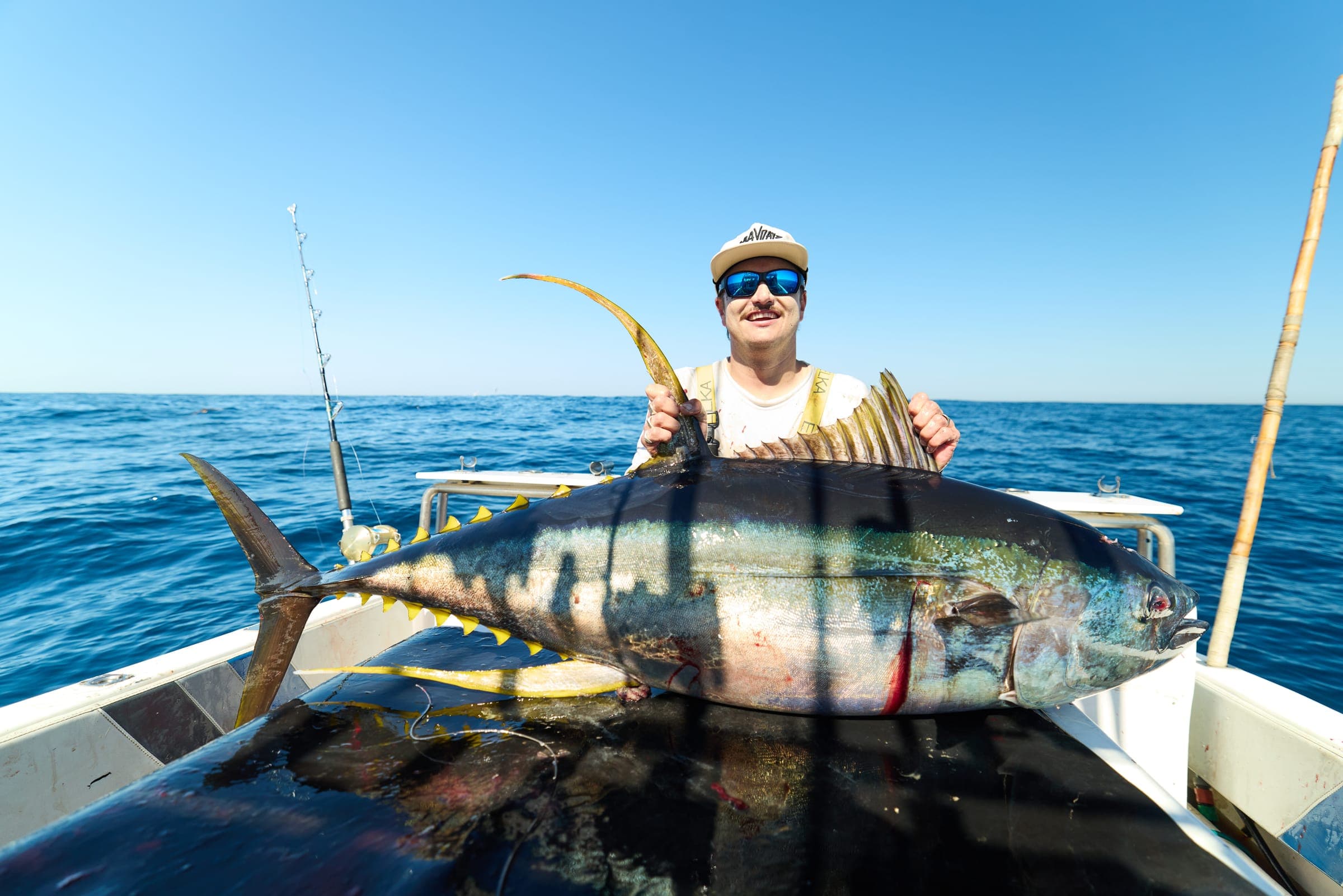 An angler holding a yellowfin tuna across the gunwale, with rods standing in their holders behind.