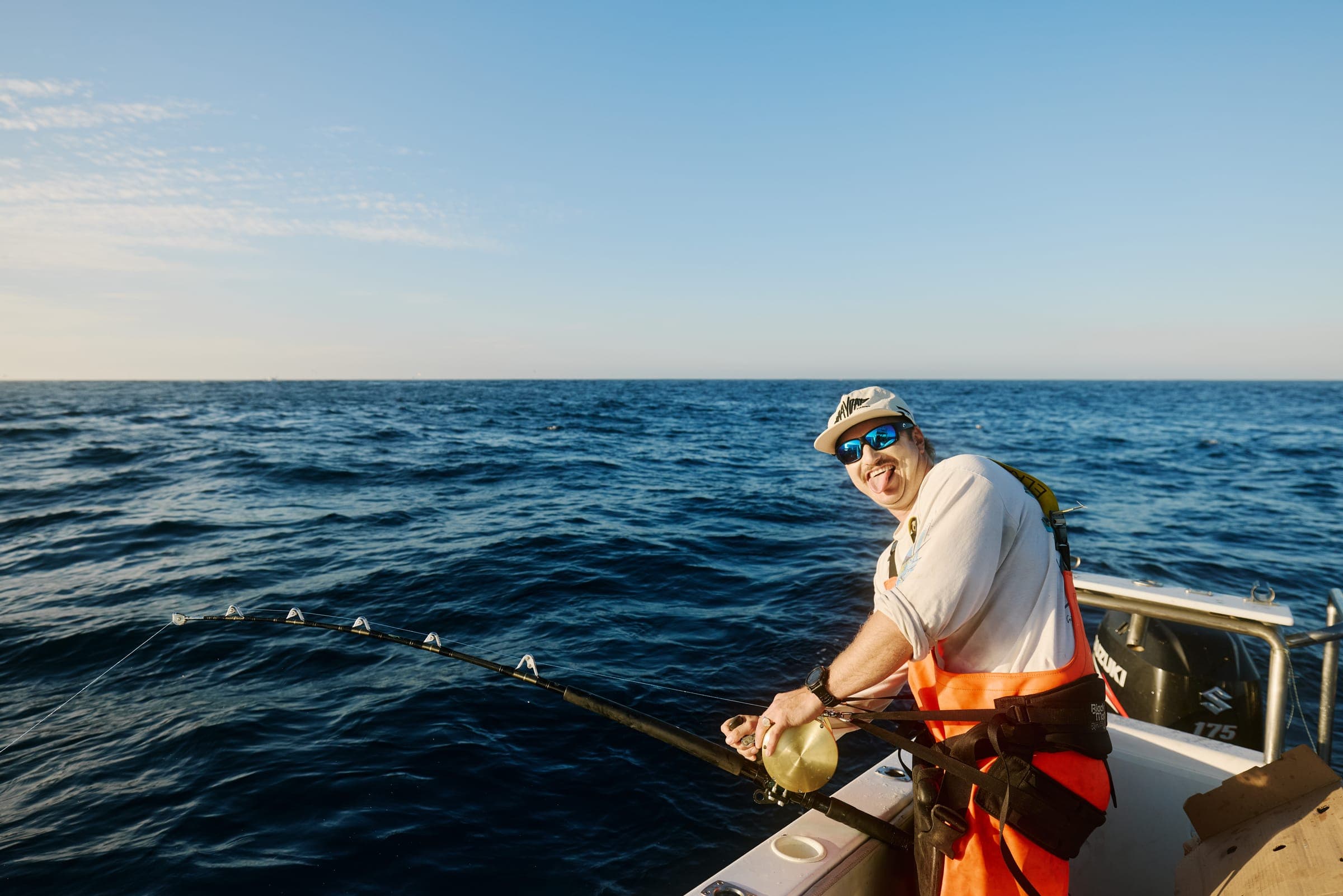 An angler working a rod at the rail in late afternoon light, with a clear horizon behind.