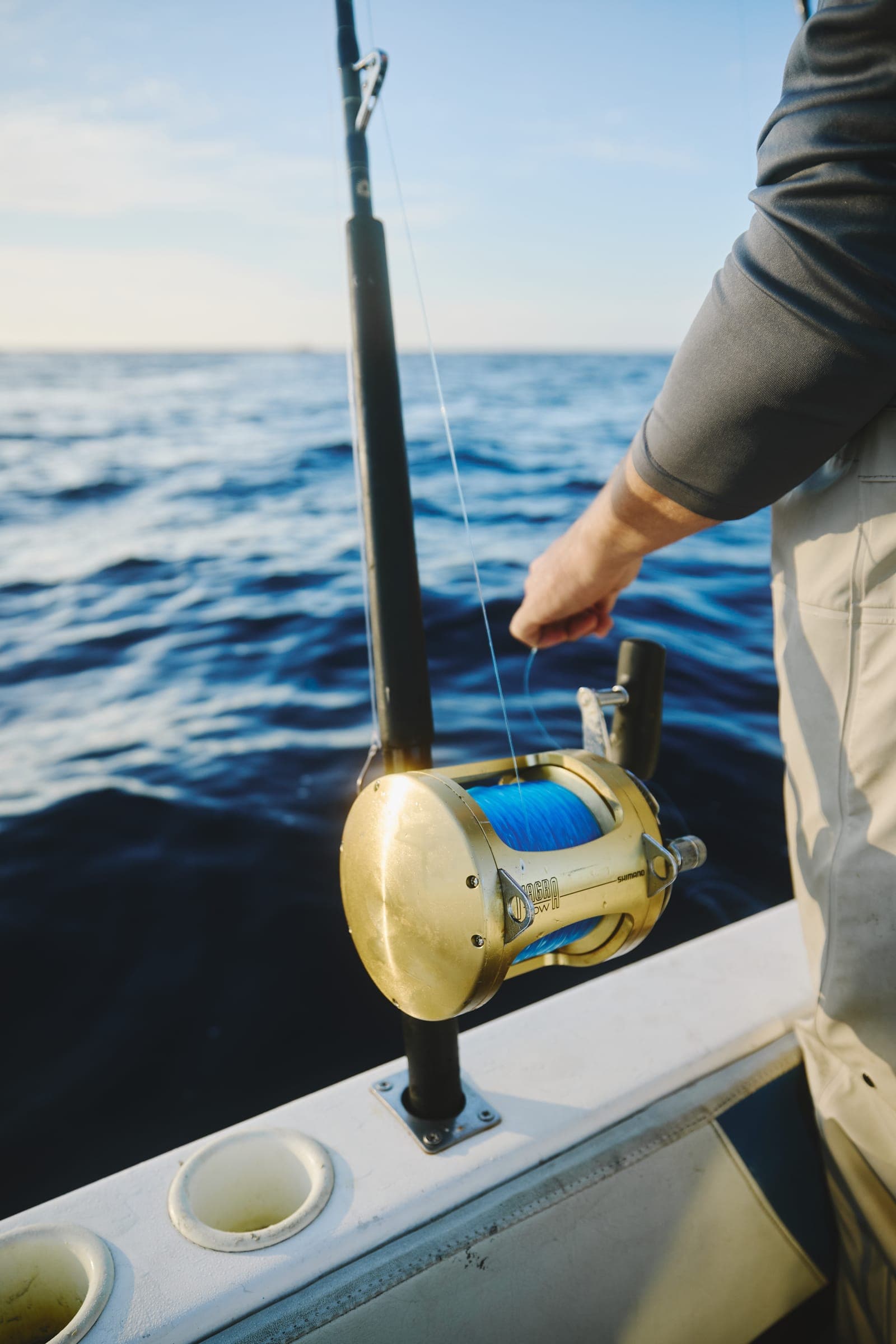 Close detail of a gold two-speed lever-drag reel mounted on a stand-up rod at the gunwale.