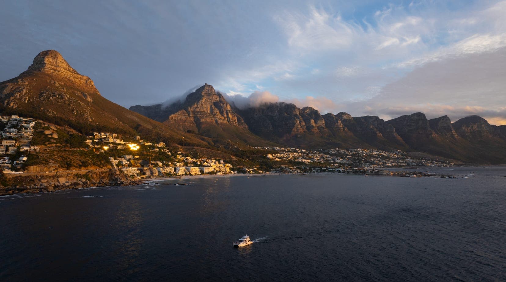 Lion’s Head, Table Mountain and the Twelve Apostles at golden hour above Camps Bay, with a single boat running the coastline below.