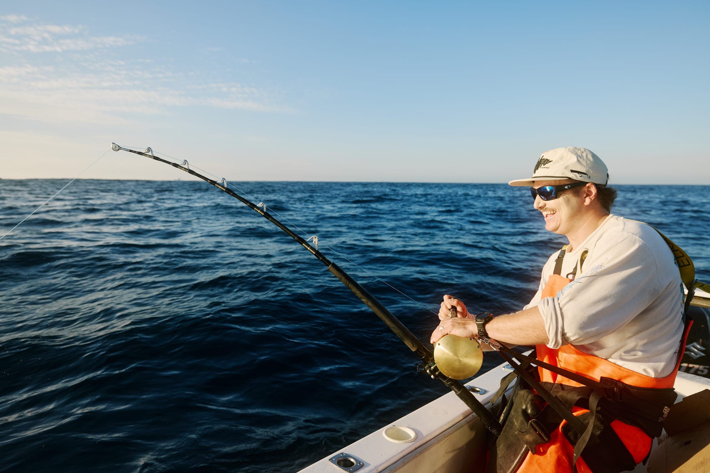 A first-time angler sitting at the rail with a rod in hand on a flat, blue morning.